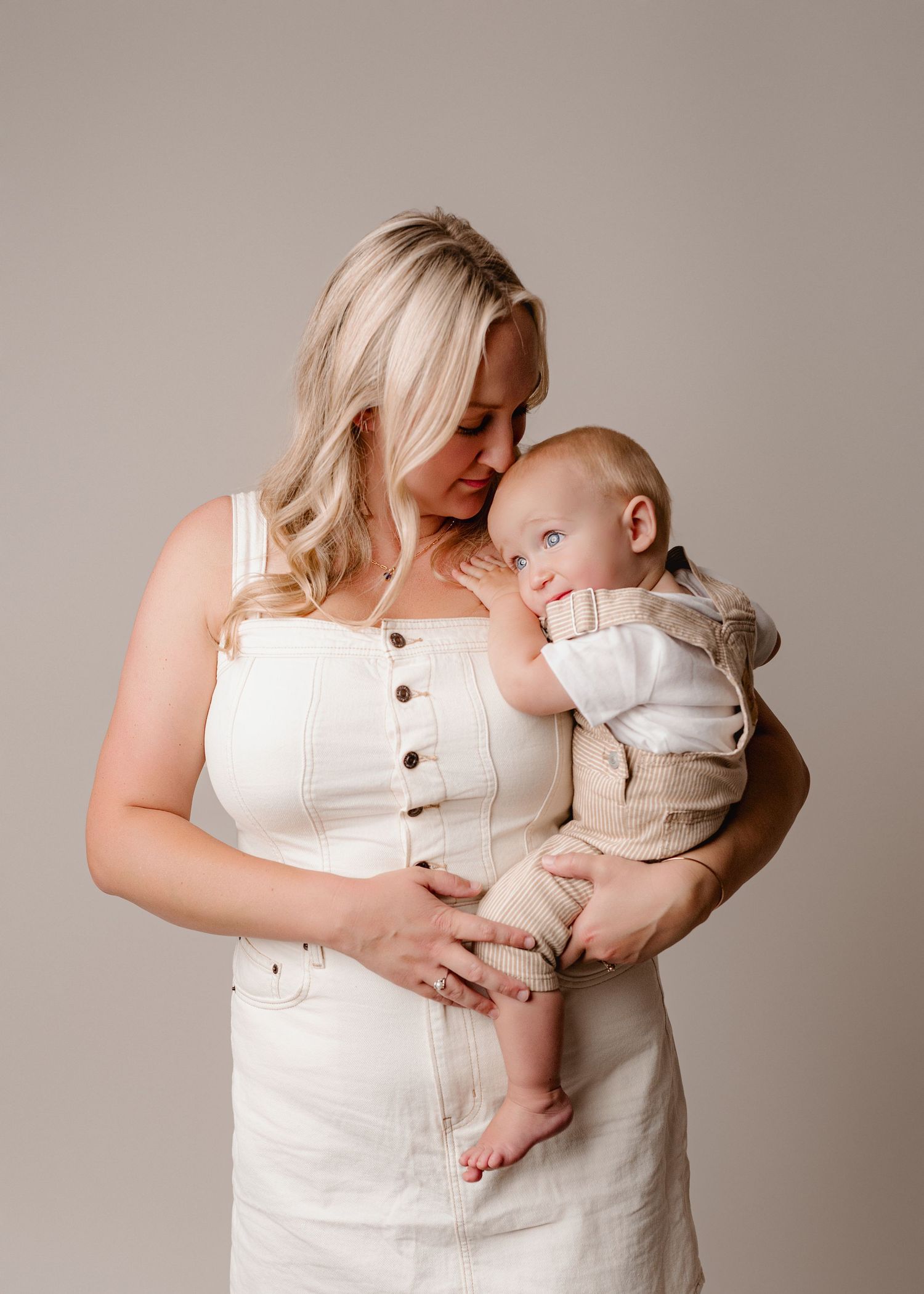 A tender moment captured in a series of four photos showing a parent and baby in matching white outfits against a neutral backdrop.