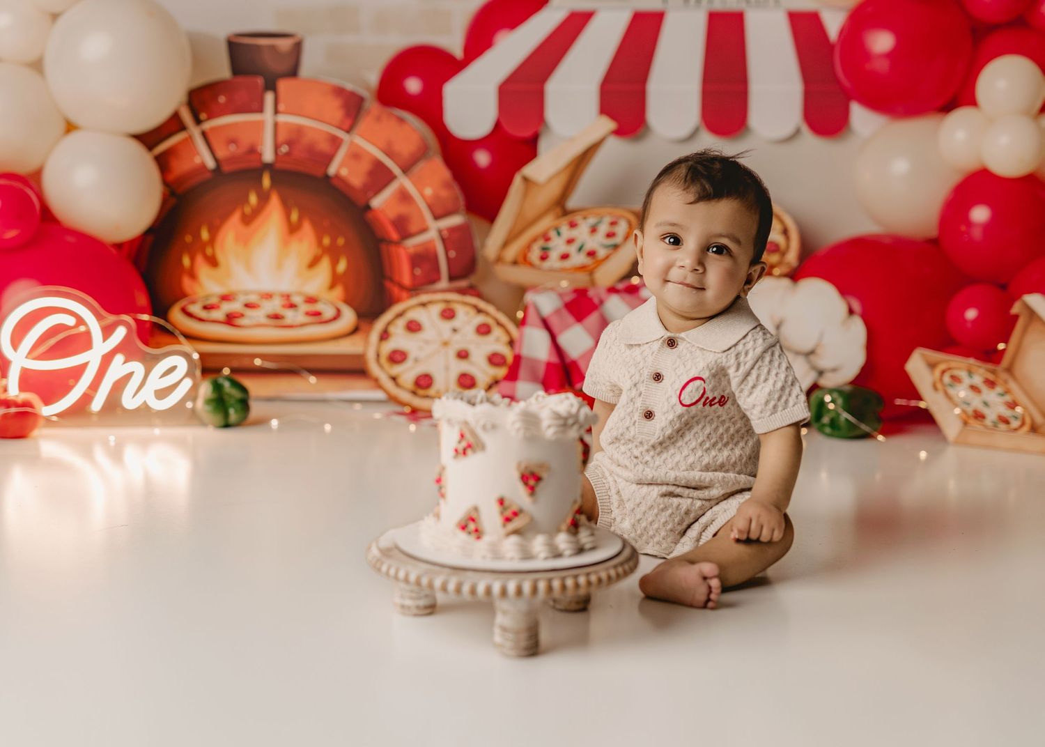 Baby's first birthday cake smash with pizza theme, red balloons, and decorative backdrop celebrating turning one.