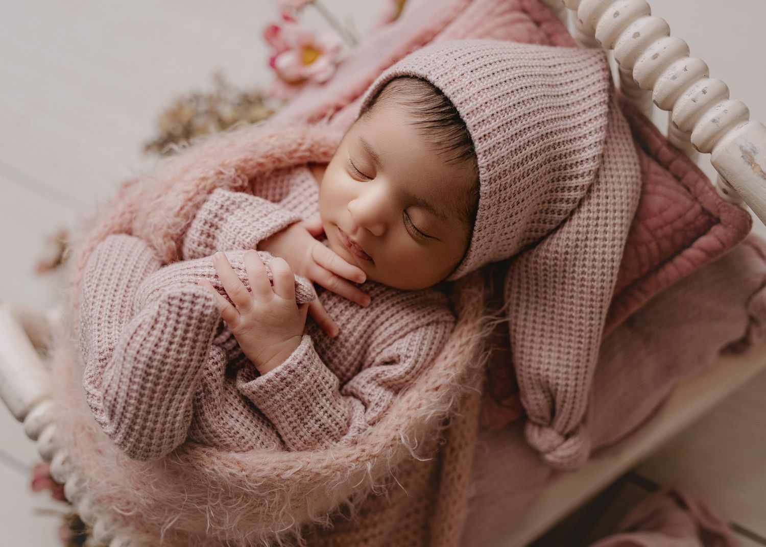 Newborn baby wearing pink knit outfit sleeping peacefully on soft textured blanket in natural light.