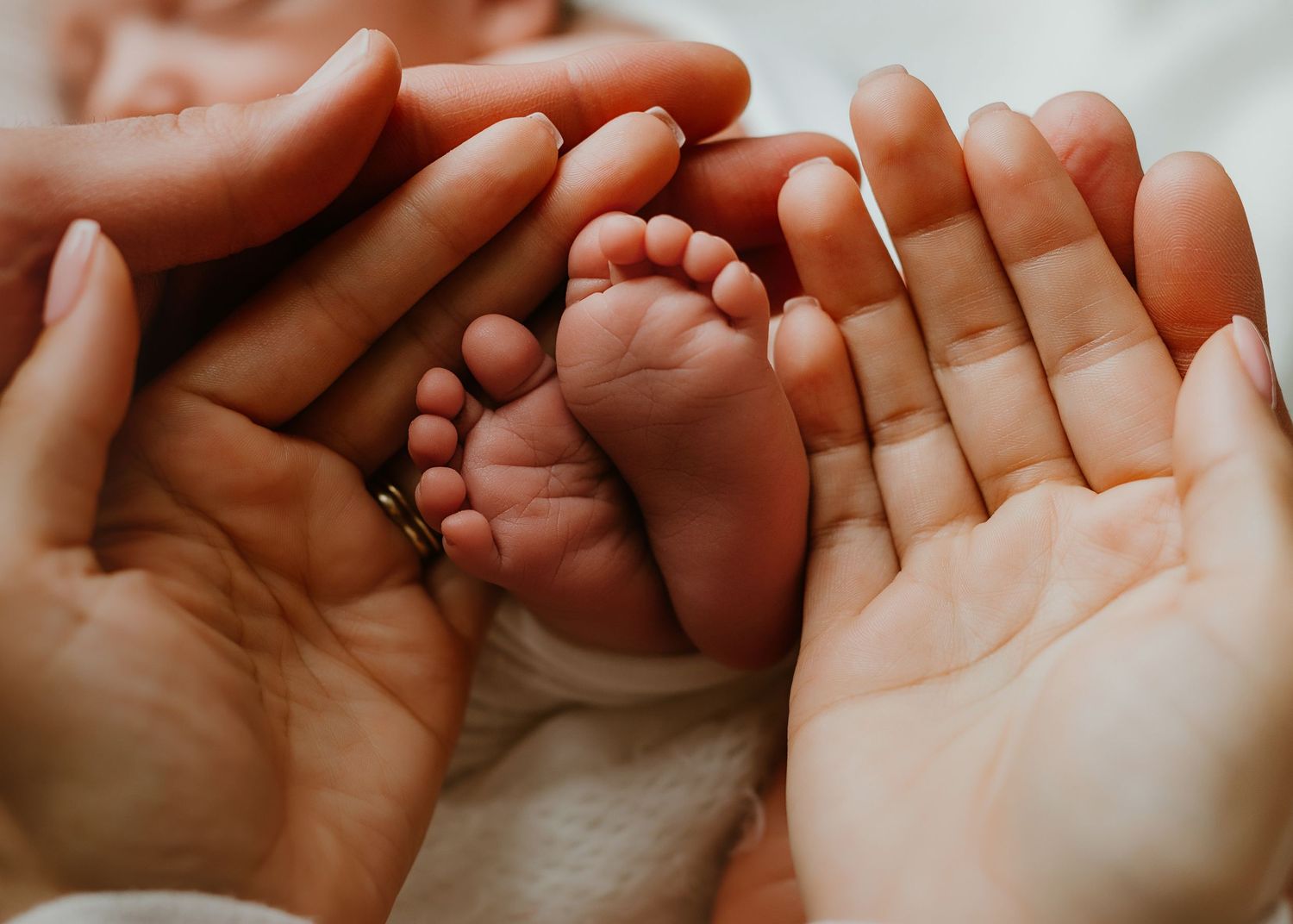 Two adult hands cradling tiny newborn baby feet, symbolizing love and new parenthood.