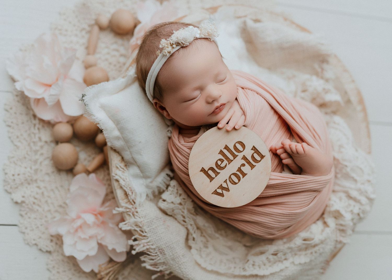 Sleeping newborn baby wrapped in pink swaddle with hello world wooden sign in a cozy basket.