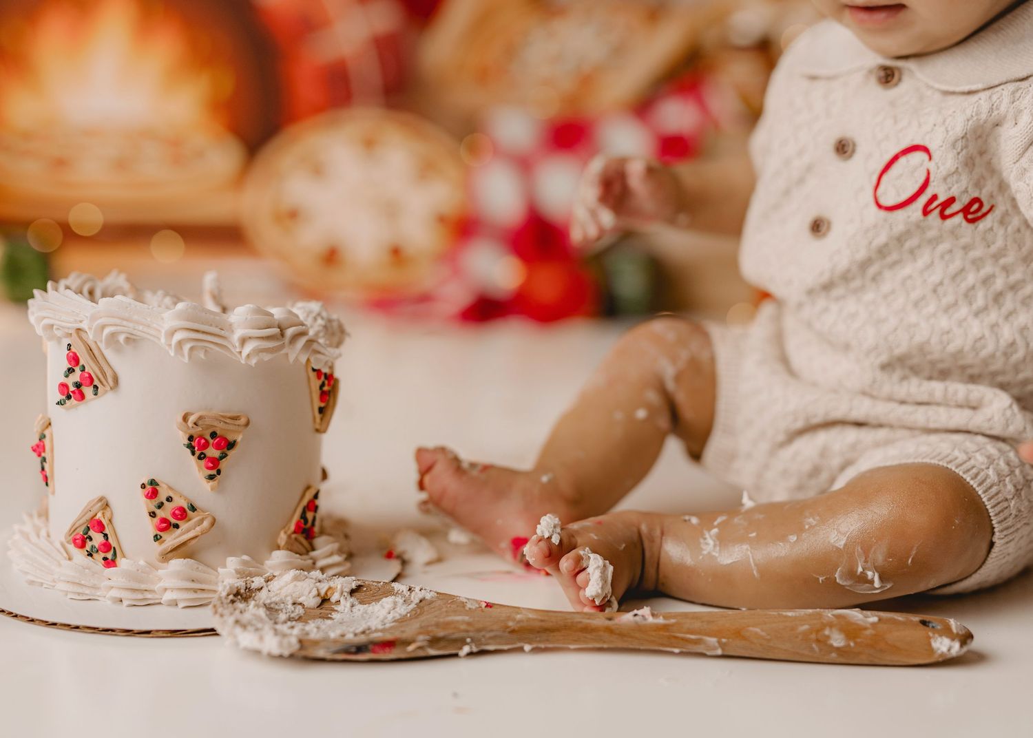 Baby in white romper smashing a pizza-themed first birthday cake, with frosting mess on floor.