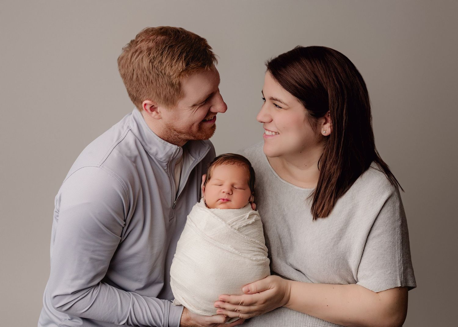 A series of five neutral-toned studio portraits showing tender family moments with a newborn baby.