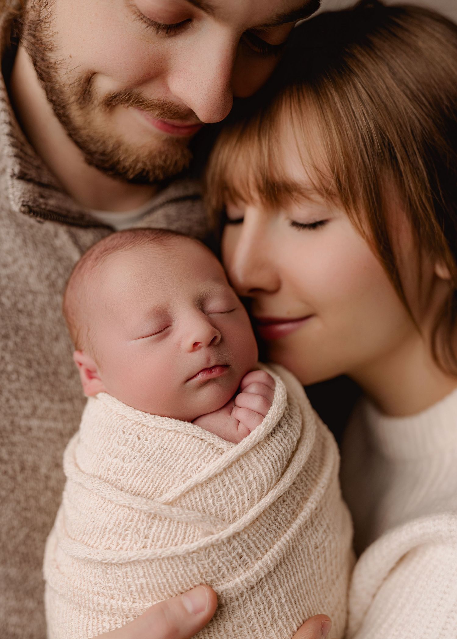 A tender moment captured in warm tones showing a parent and sleeping baby in matching cream knit sweaters.