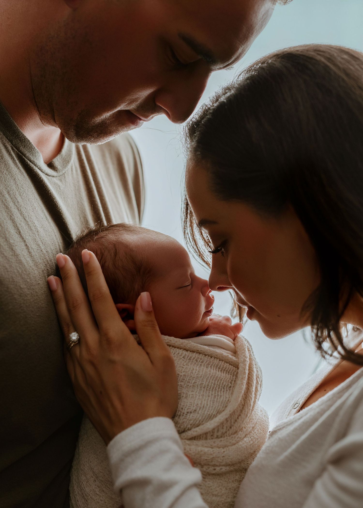 Two parents tenderly holding their newborn baby, sharing an intimate family moment in soft warm lighting.