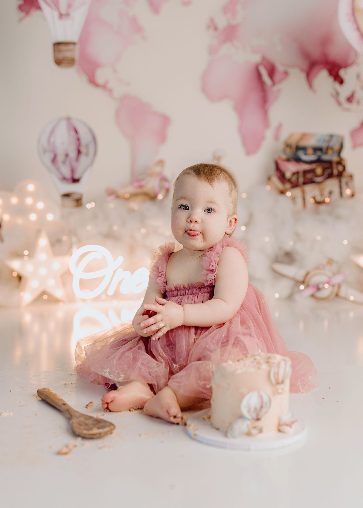 Baby in pink tutu dress sits beside smashed first birthday cake with hot air balloon backdrop. Southeast Michigan cake smash photographer