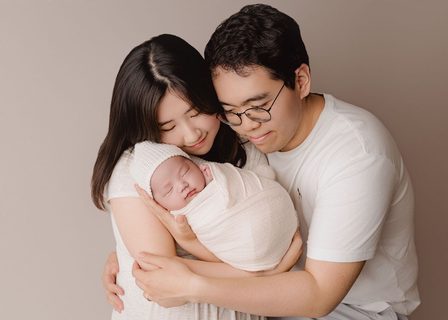 A series of tender parental moments showing gentle embraces and bonding with a newborn baby against a neutral backdrop.
