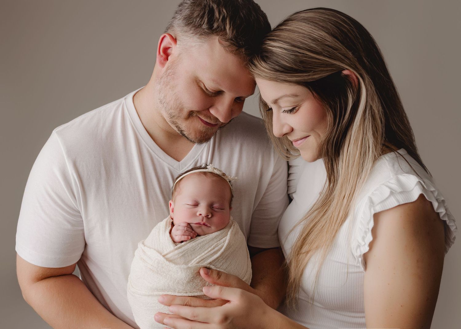 Parents in white shirts share tender moments with their newborn baby in a series of intimate studio portraits.