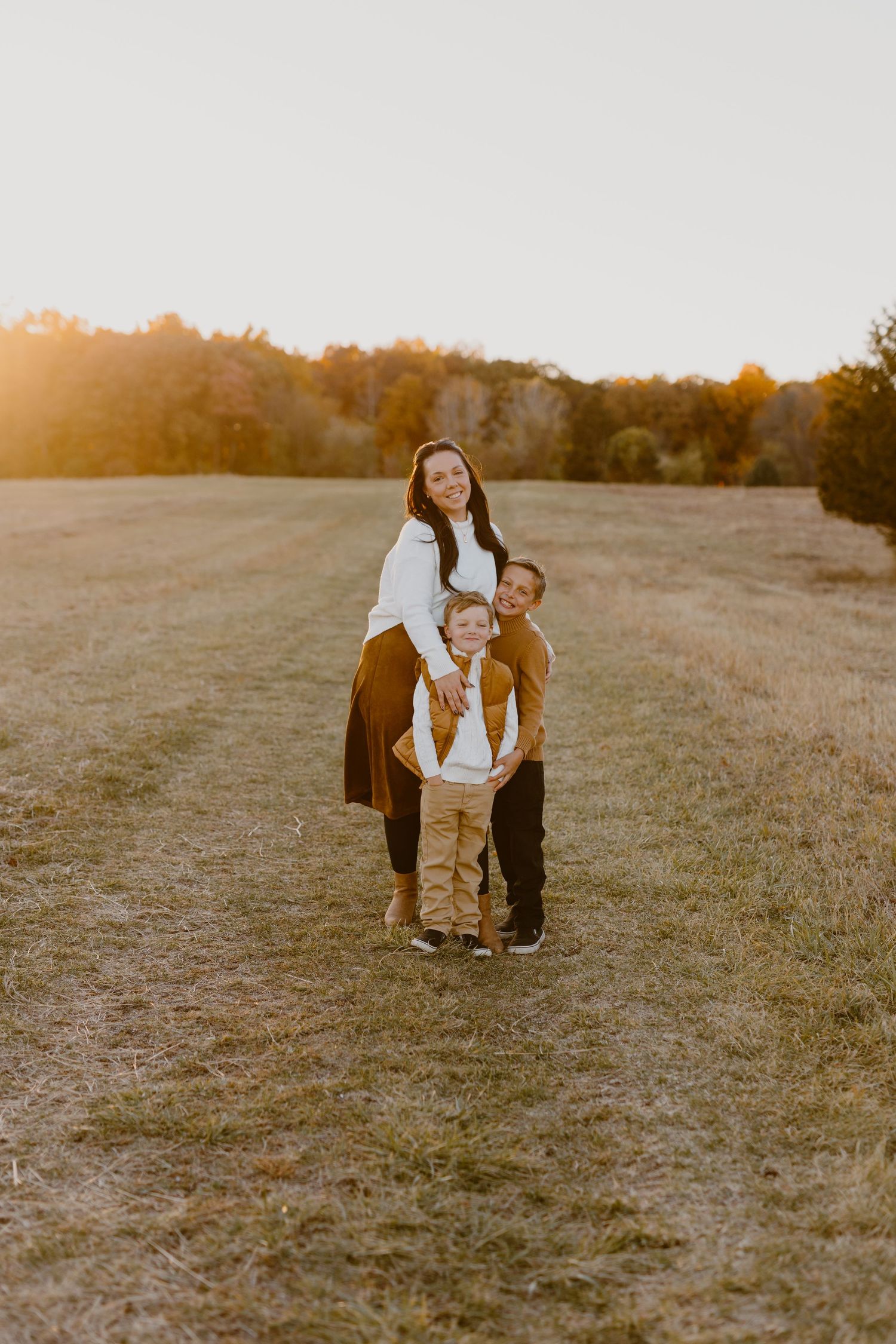 A family shares tender moments together in a golden field at sunset, creating heartwarming candid photographs.