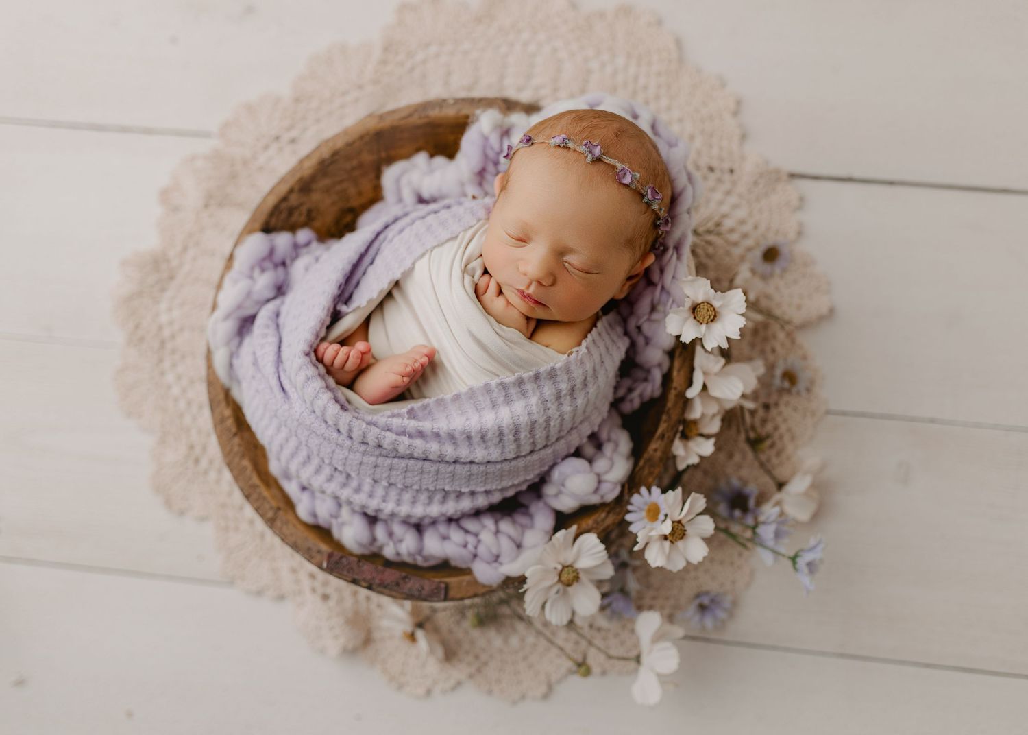 Newborn baby girl sleeping in a wooden bowl wrapped in lavender, with a floral headband and daisy decorations in Oakland County, Michigan.