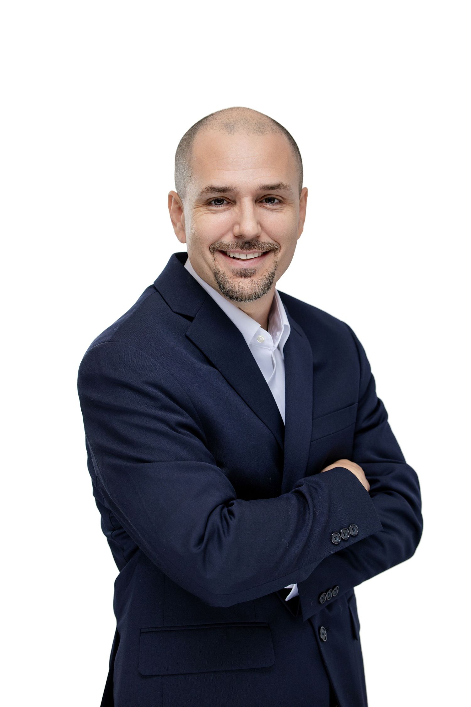 Smiling bald businessman in navy blue suit with arms crossed posing confidently against white background.