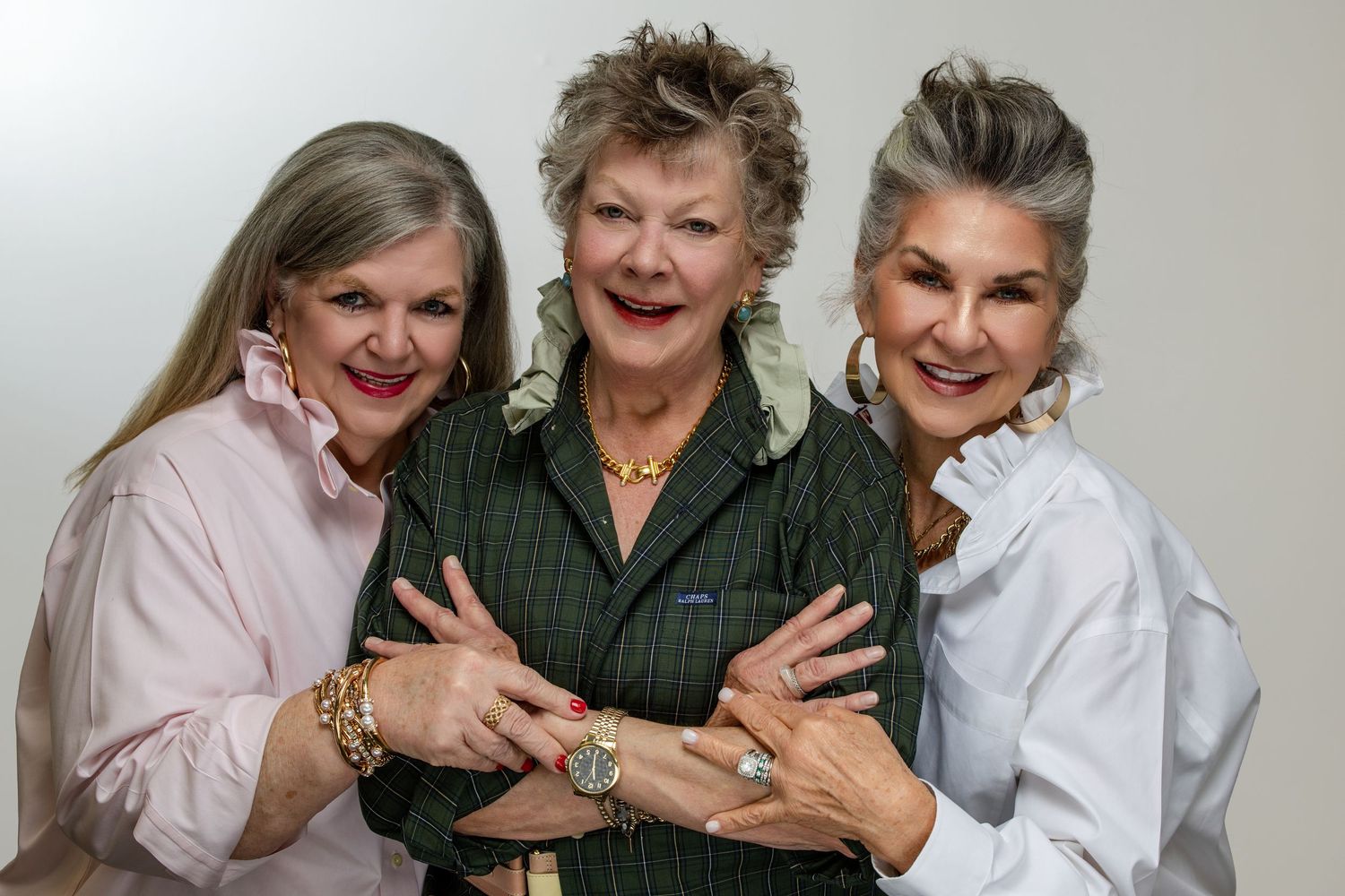 Three elegantly dressed older women smiling and posing together, wearing stylish jewelry and fashionable outfits.