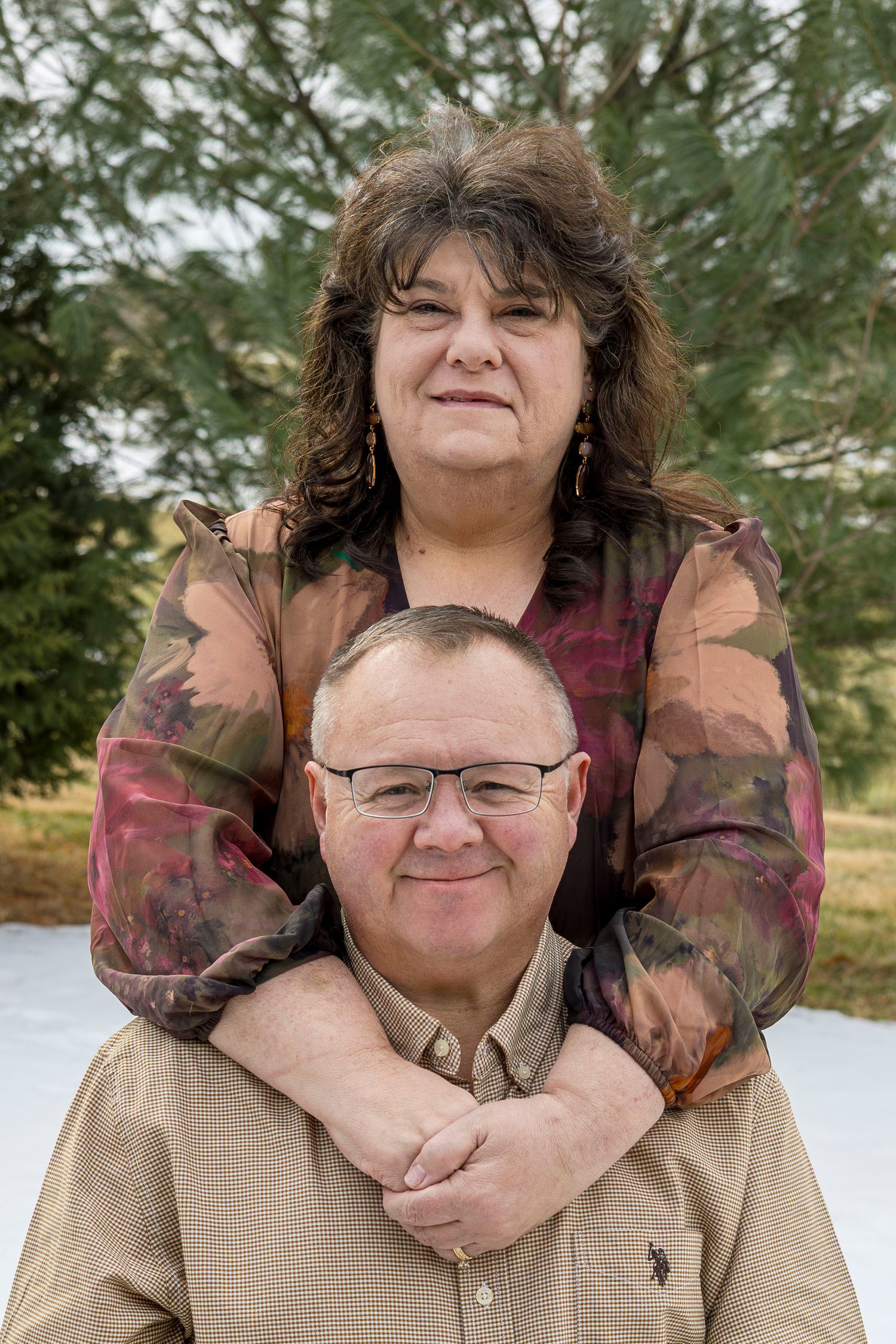 A couple embraces in a snowy outdoor setting while wearing casual winter clothing.