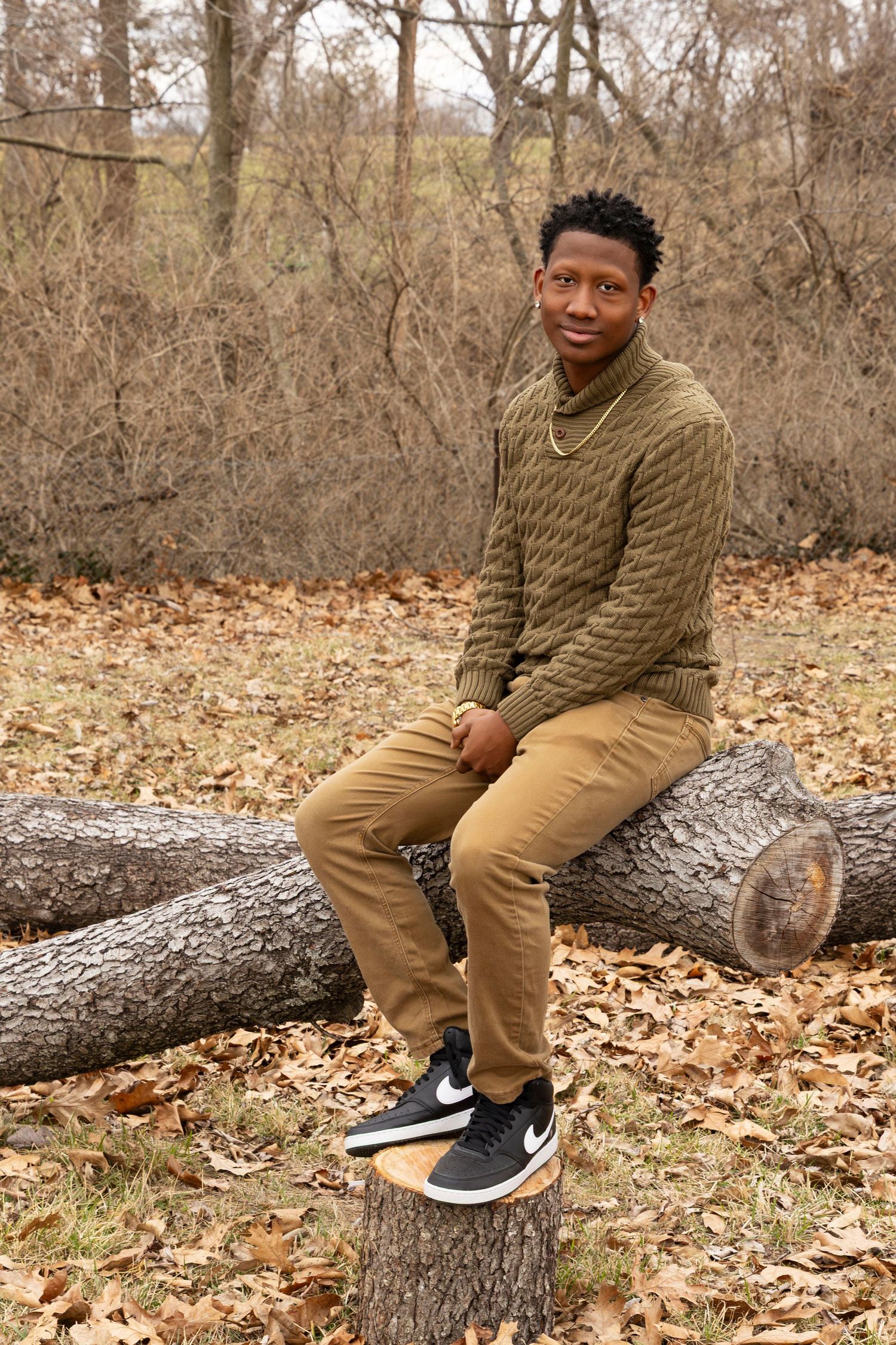 A person in brown clothing sits on a fallen tree trunk surrounded by autumn leaves in a forest setting.