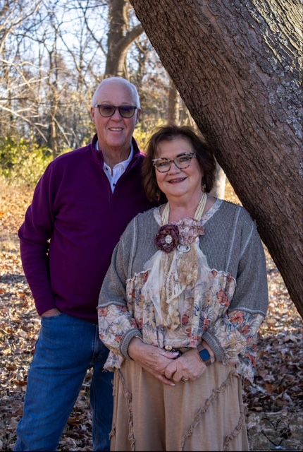 A couple poses together under a large tree trunk in an autumn woodland setting.