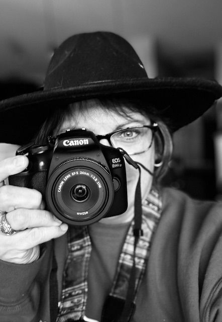 Dramatic black and white close-up of a Canon camera lens and photographer wearing a hat.