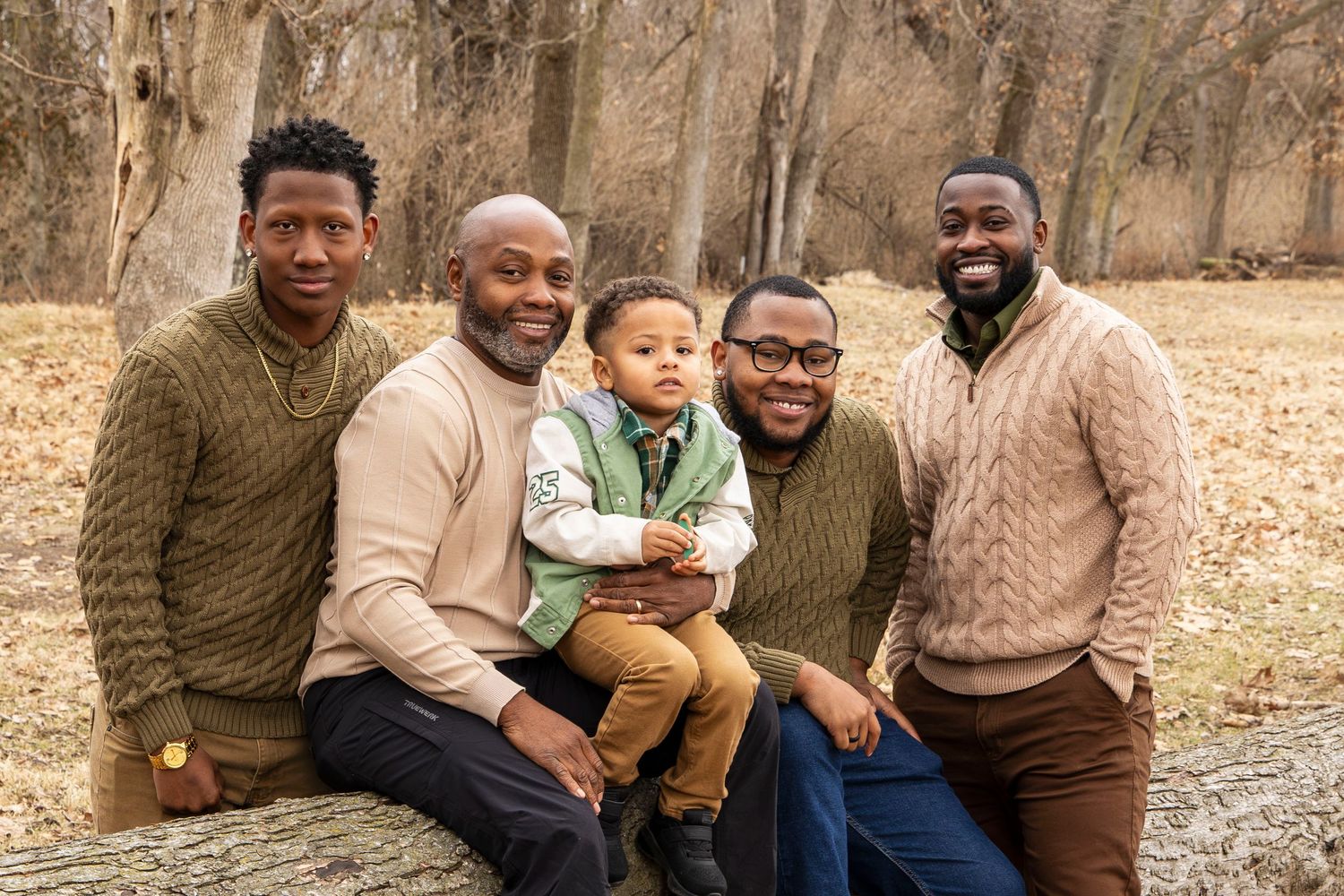 A group of people wearing earth-toned sweaters pose together outdoors during autumn.