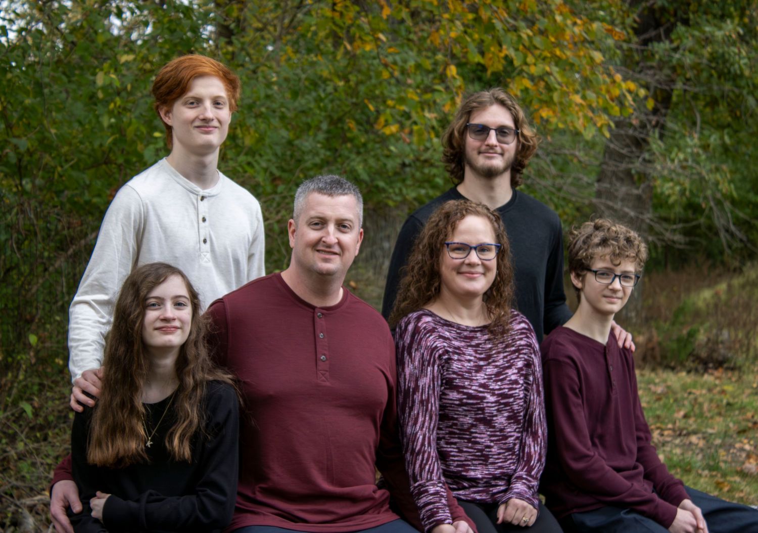 Family of six posing outdoors in autumn, smiling together among colorful fall foliage.