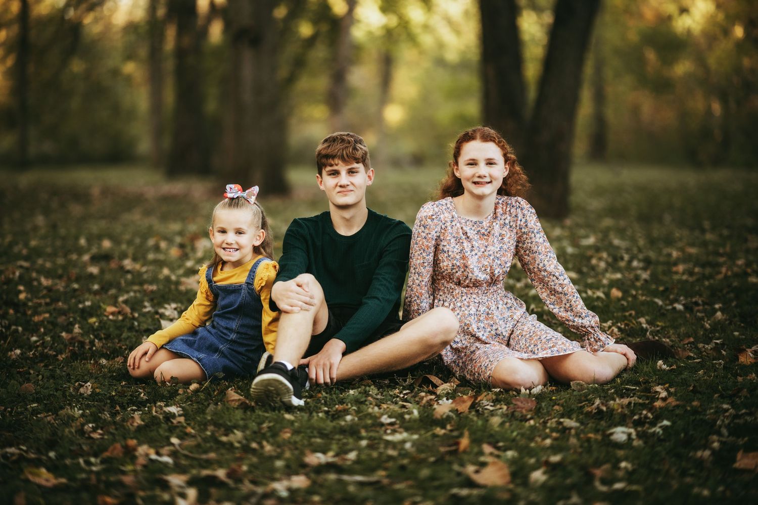 Family relaxes together on fallen autumn leaves by scenic lake during outdoor photo session.