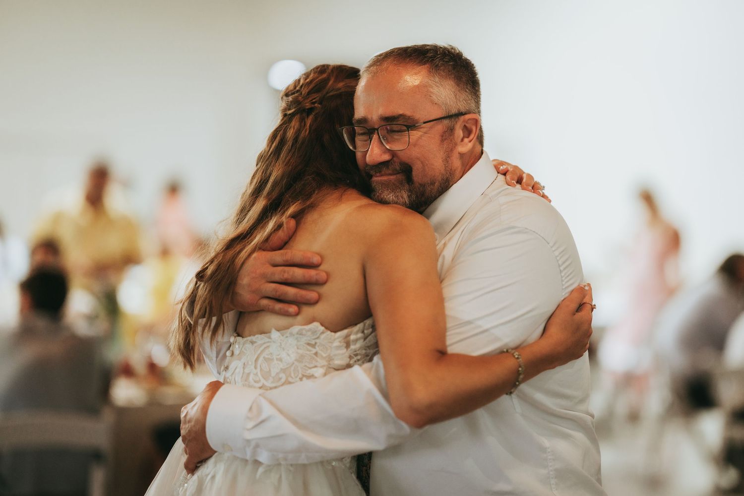 Bride and older man sharing warm embrace during father-daughter dance at wedding reception.