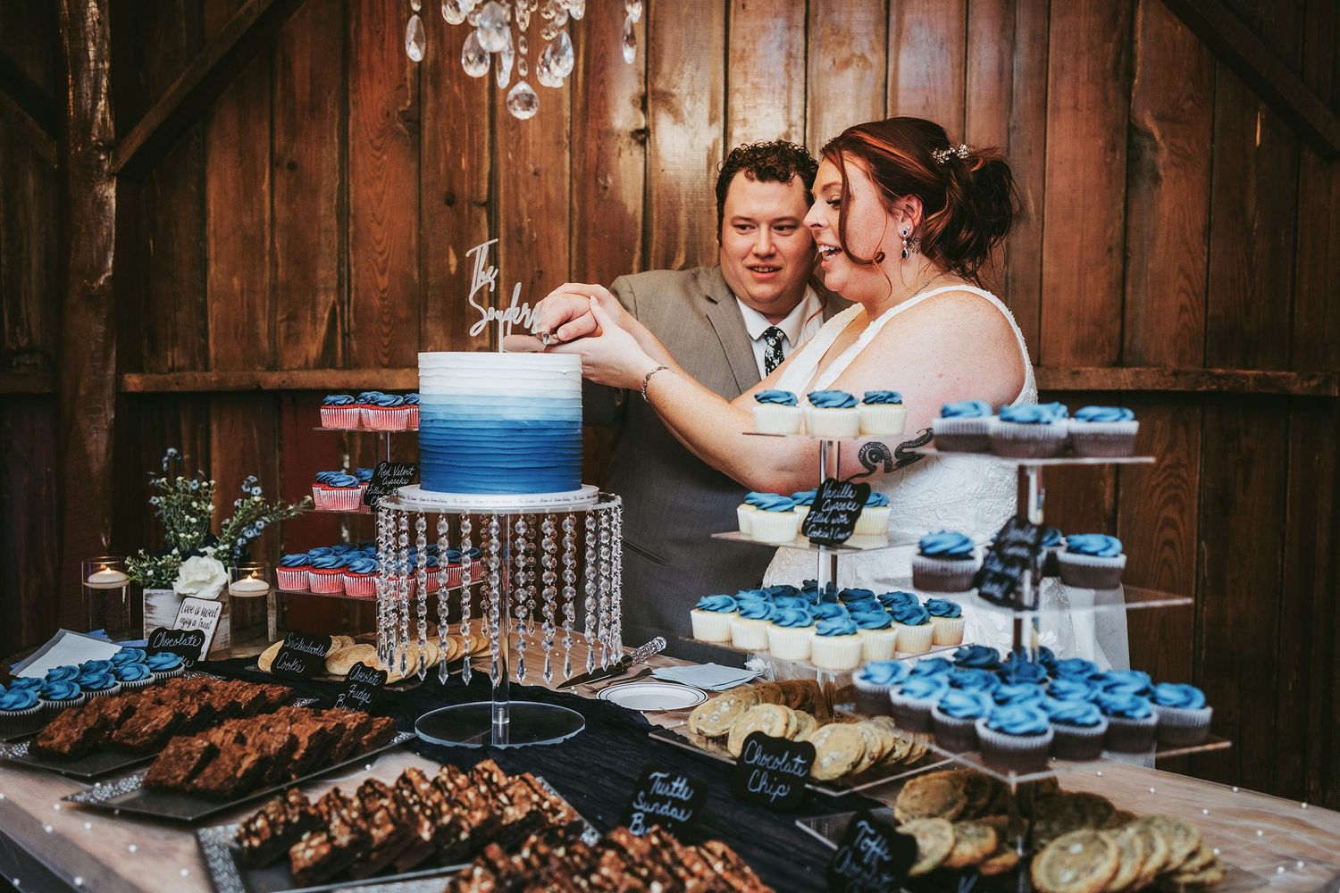 Elegant dessert display featuring a blue ombre cake and cupcakes at a rustic wooden venue.