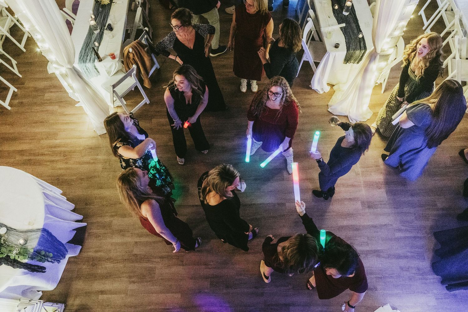 Overhead view of wedding guests dancing on a wooden floor with colorful lighting effects.