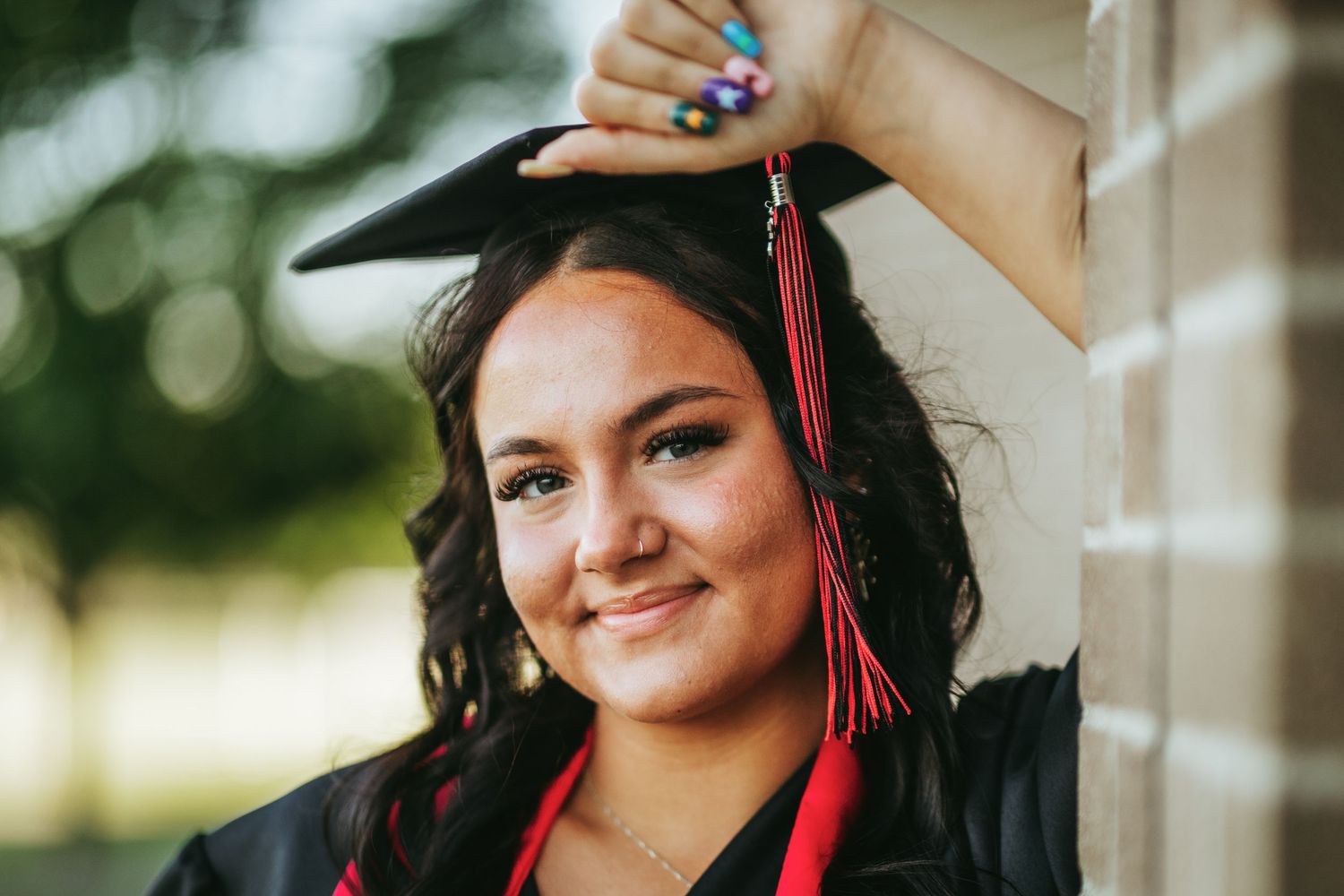 Graduate in red cap and tassel poses for a series of celebratory graduation portraits outdoors.