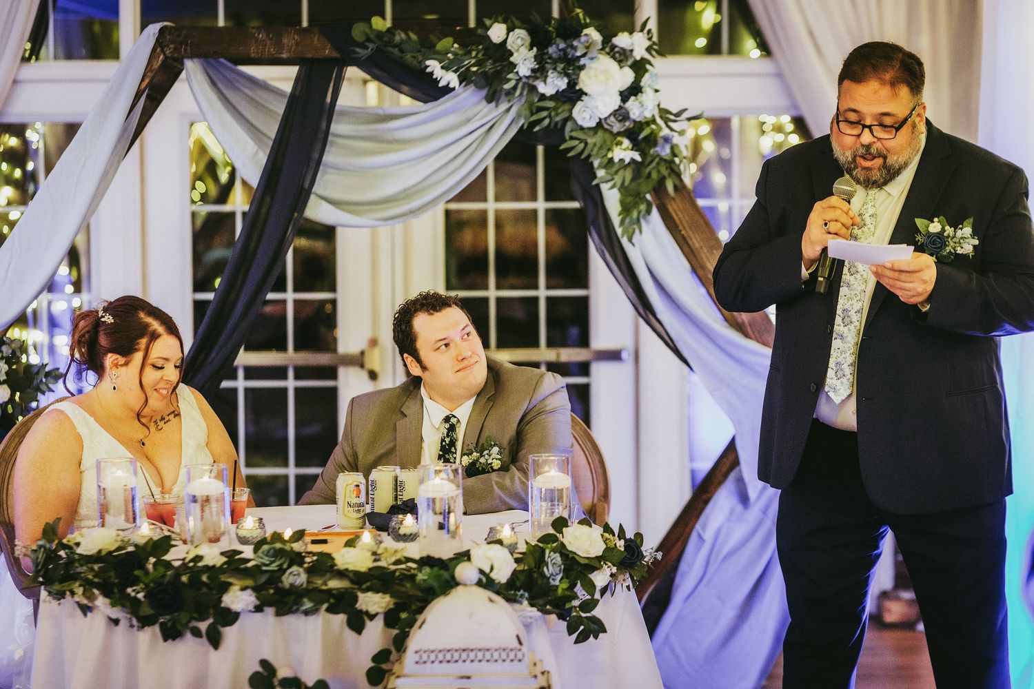 Wedding reception venue decorated with white draping and floral arrangements.