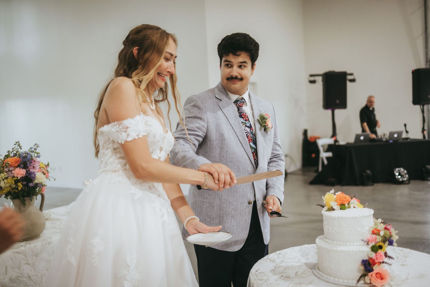Bride and groom cutting white wedding cake together at elegant indoor wedding reception.