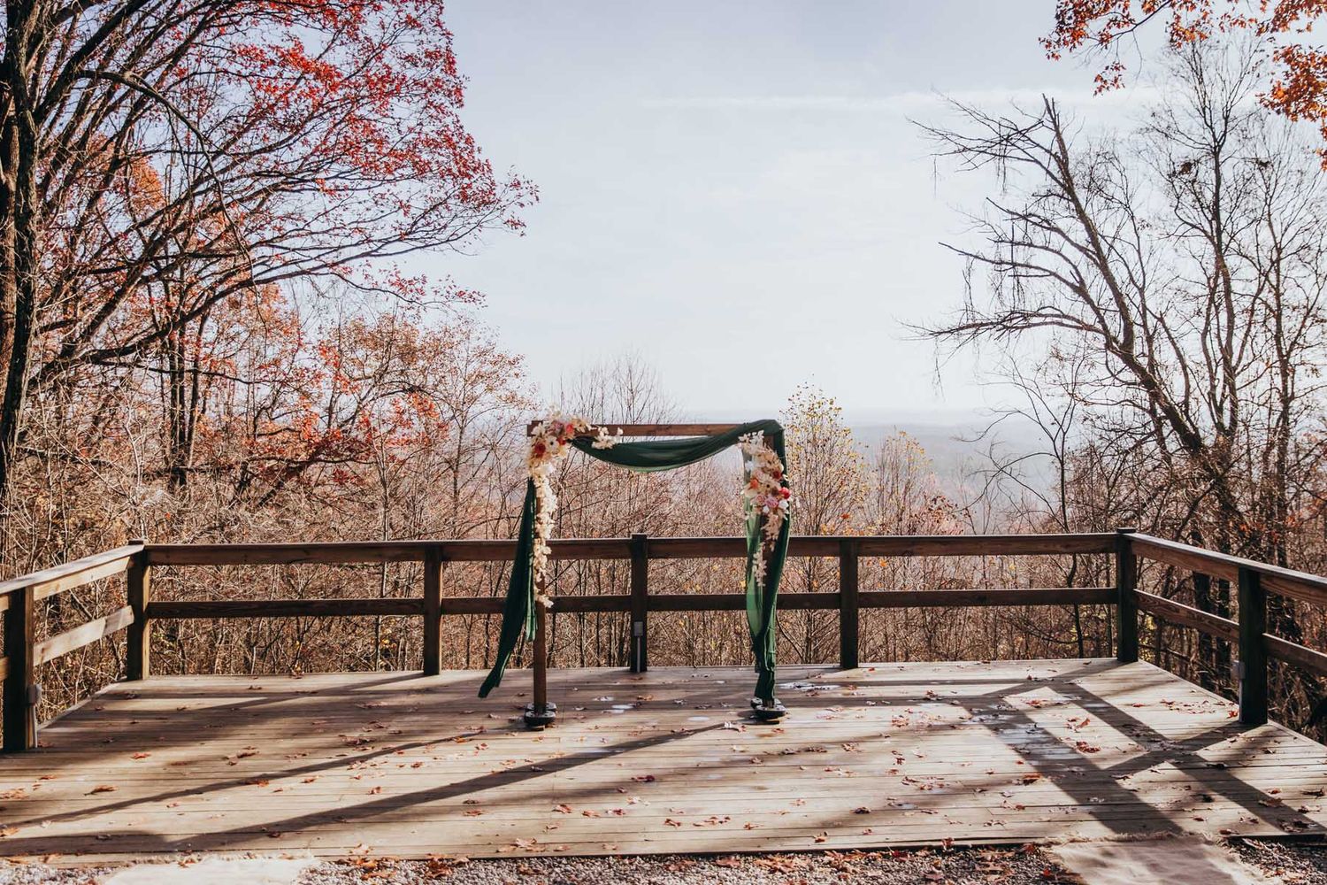 A scenic autumn boardwalk trail winds through a forest with red and orange foliage on a misty day.