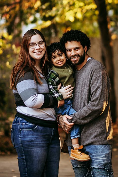 A family shares joyful moments together during an autumn photoshoot in a park with golden sunlight filtering through trees.