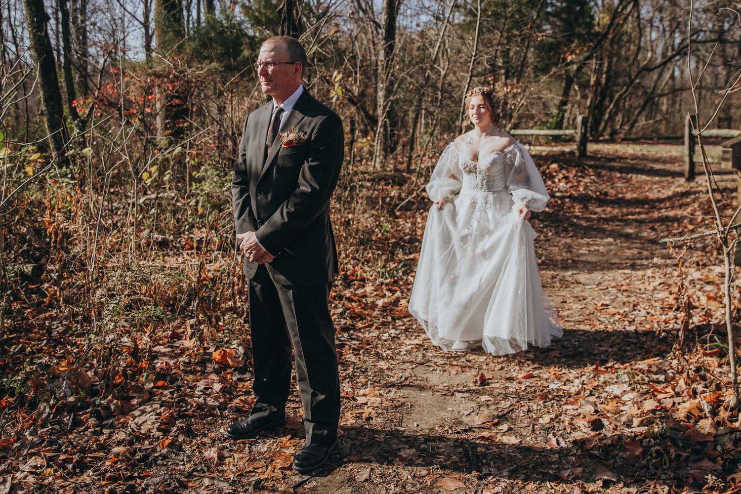 A couple shares a romantic moment in a fall forest setting with golden leaves scattered on the ground.