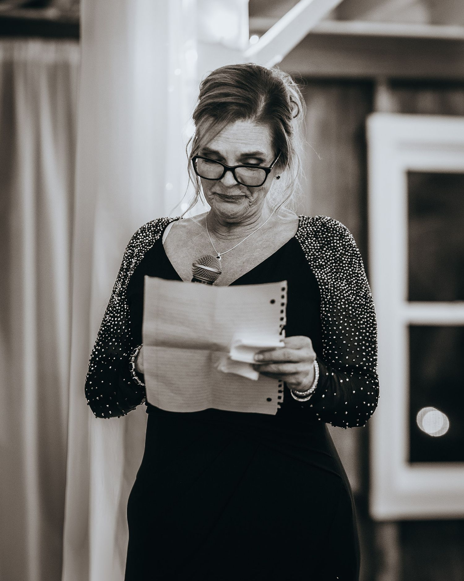 A speaker in formal attire reads from papers during an evening event.
