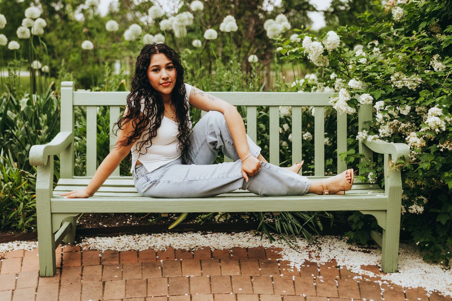 Someone relaxes on a mint green garden bench surrounded by blooming white roses in a summer garden setting.