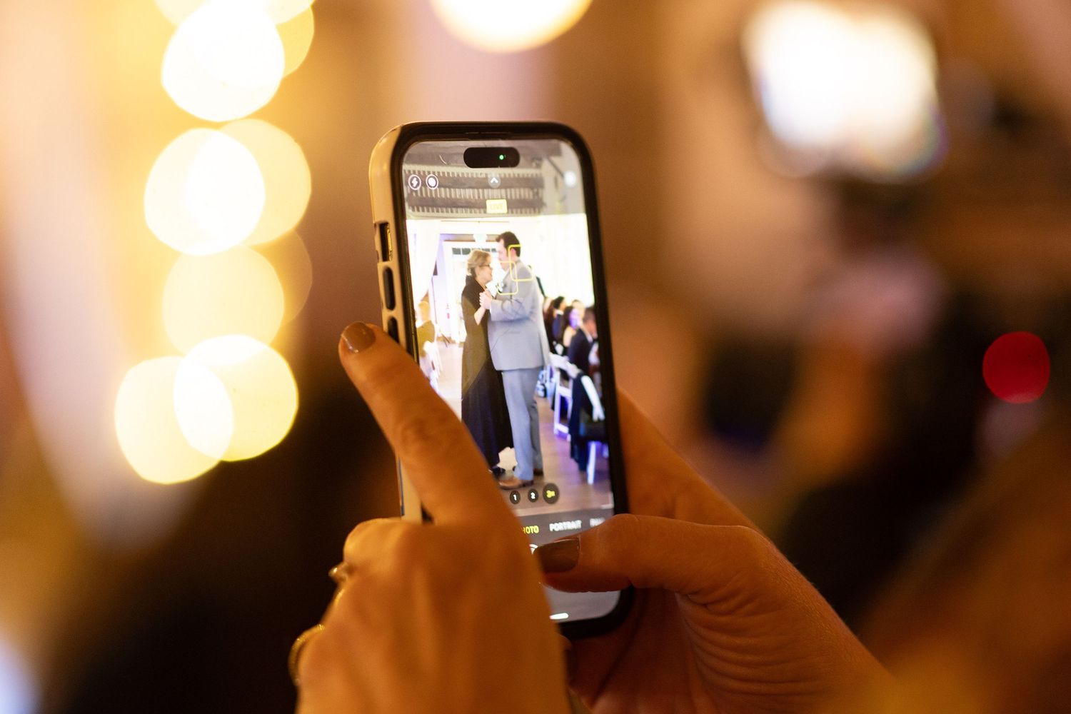 Guests taking photos with smartphones at a wedding reception with bokeh lights in background.