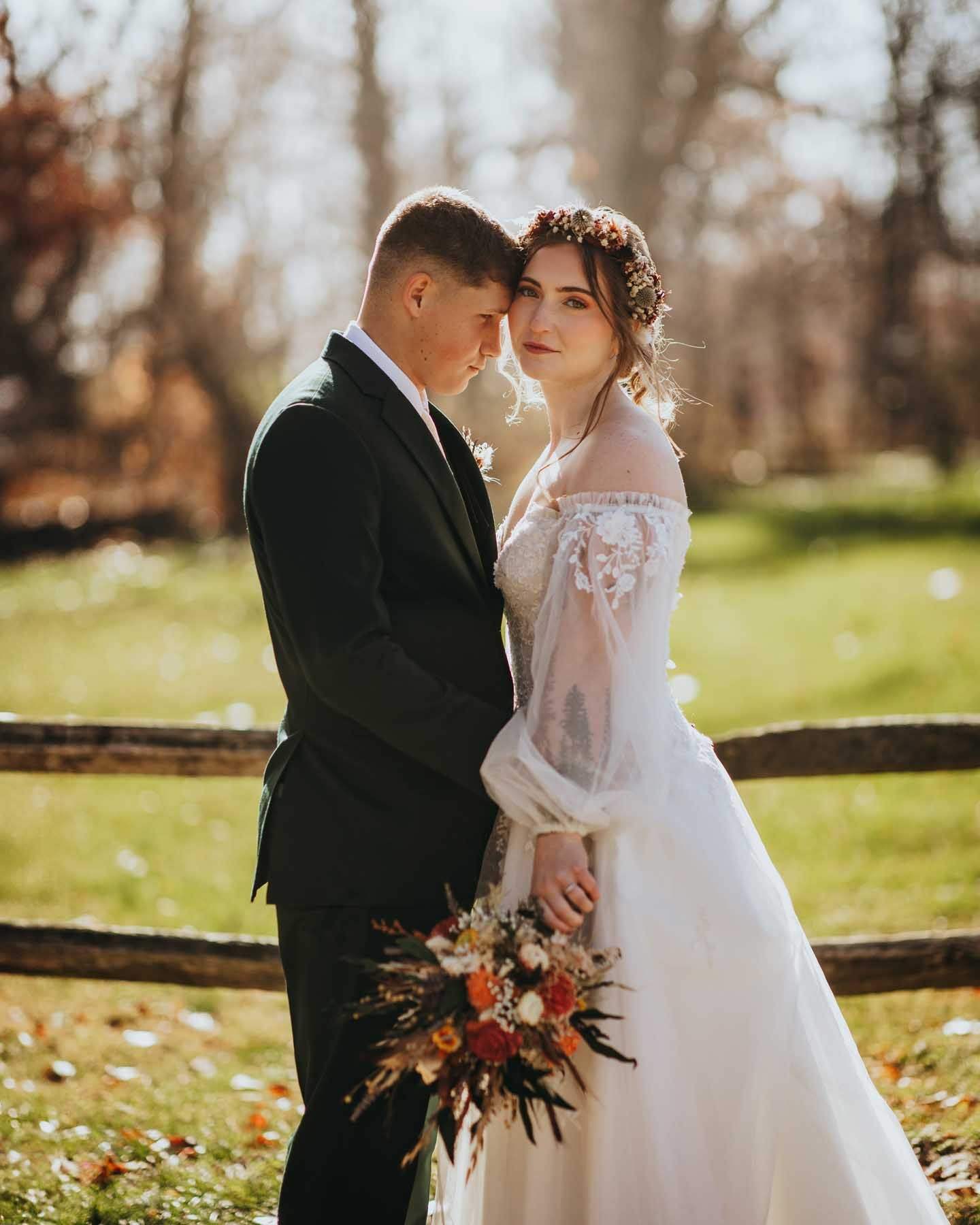 A romantic autumn wedding photo shoot featuring a couple on a grassy lawn with fall foliage in the background.