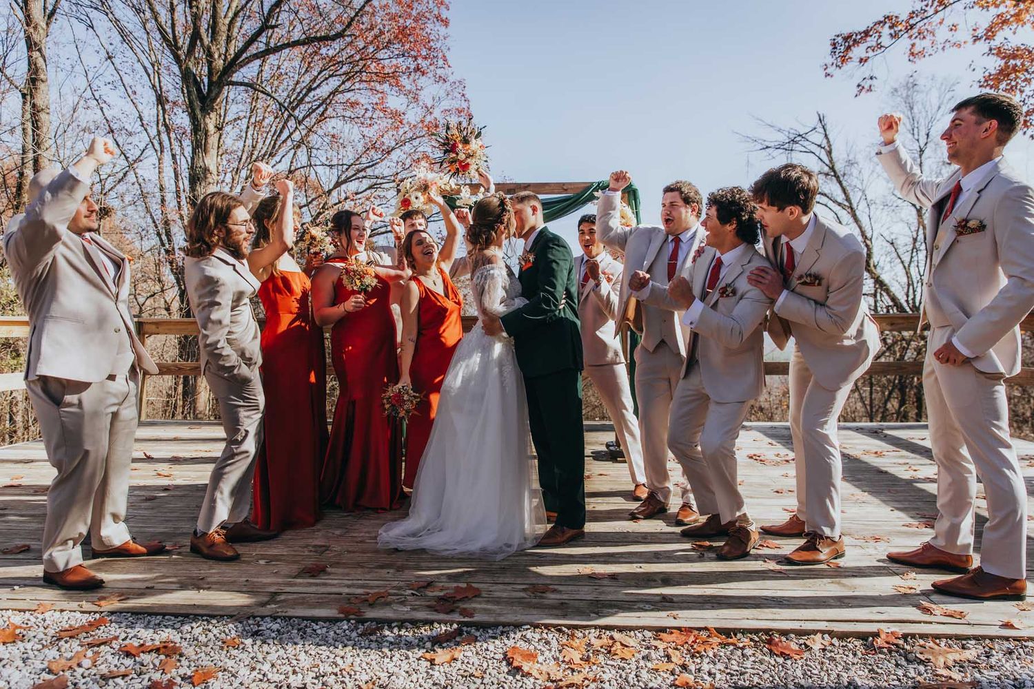 Wedding party stands in a line on stone path surrounded by autumn leaves during outdoor celebration.