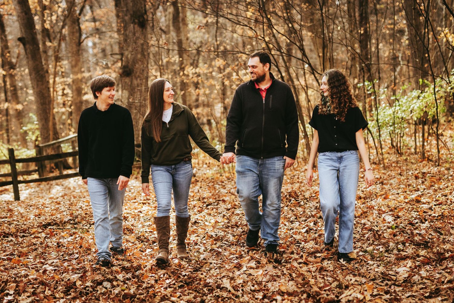 A group of friends walking together on a leaf-covered path through autumn woods.