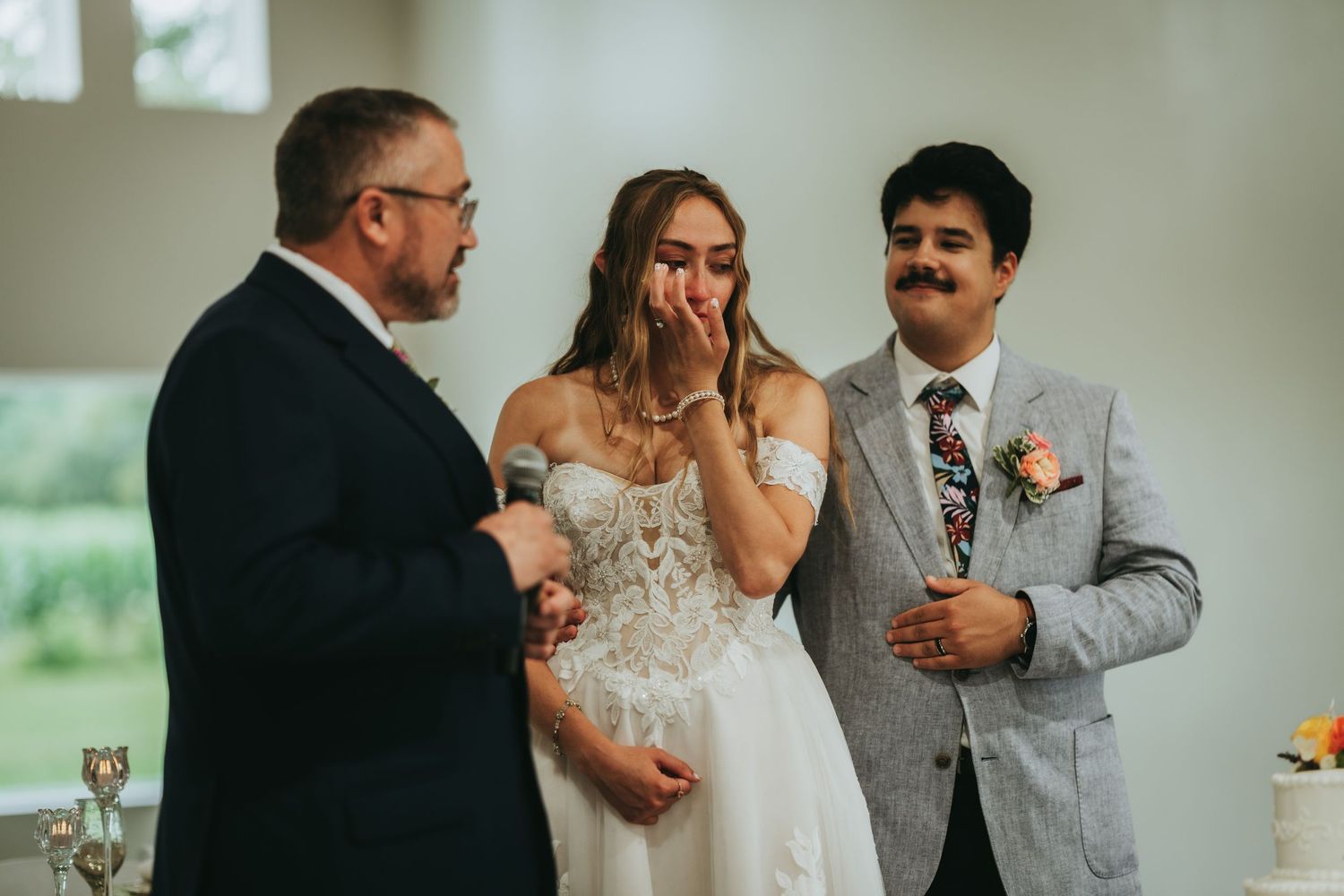 Emotional bride covers mouth in surprise while standing with groom and officiant during ceremony.