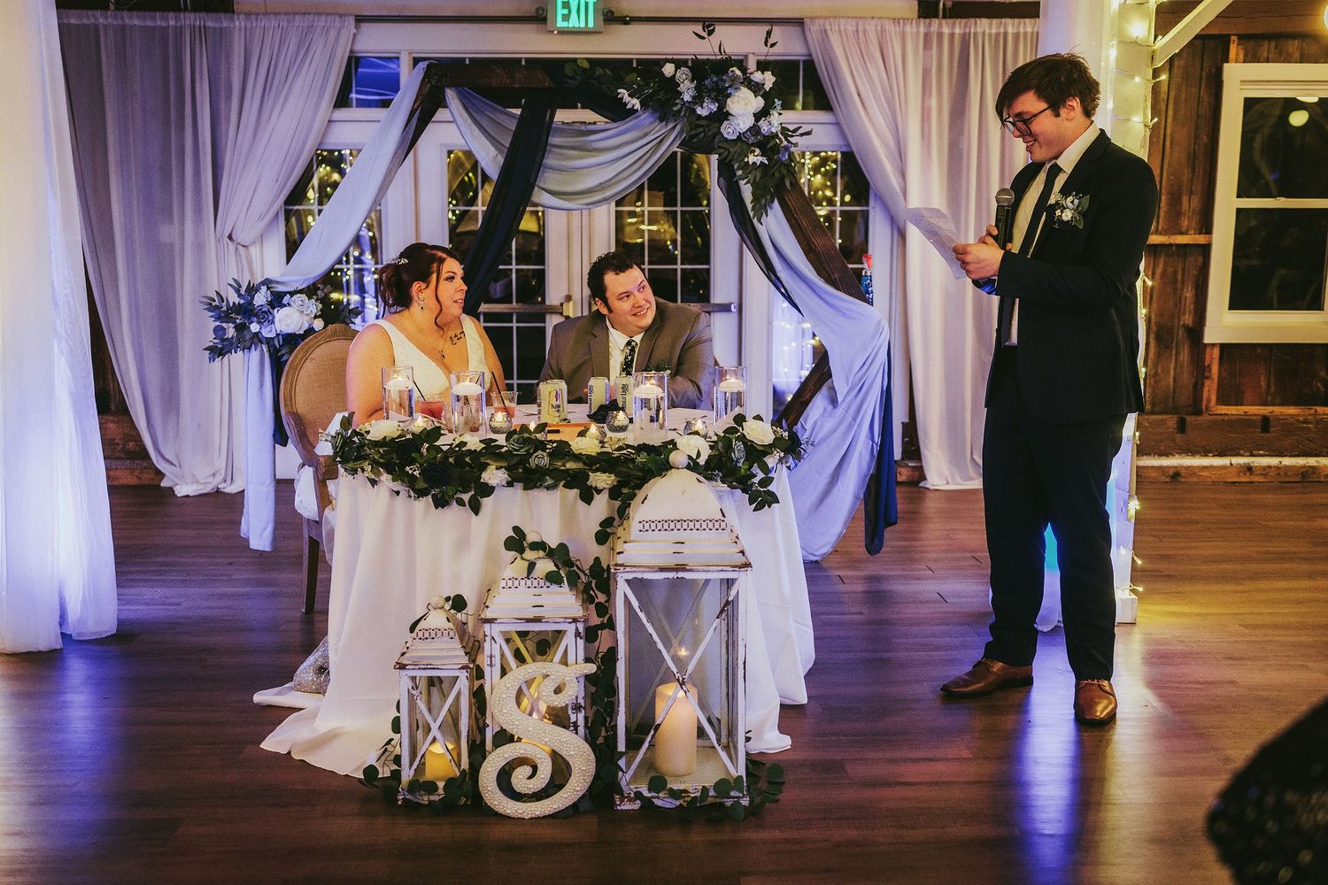 Wedding reception venue with elegant white drapes and purple ambient lighting.