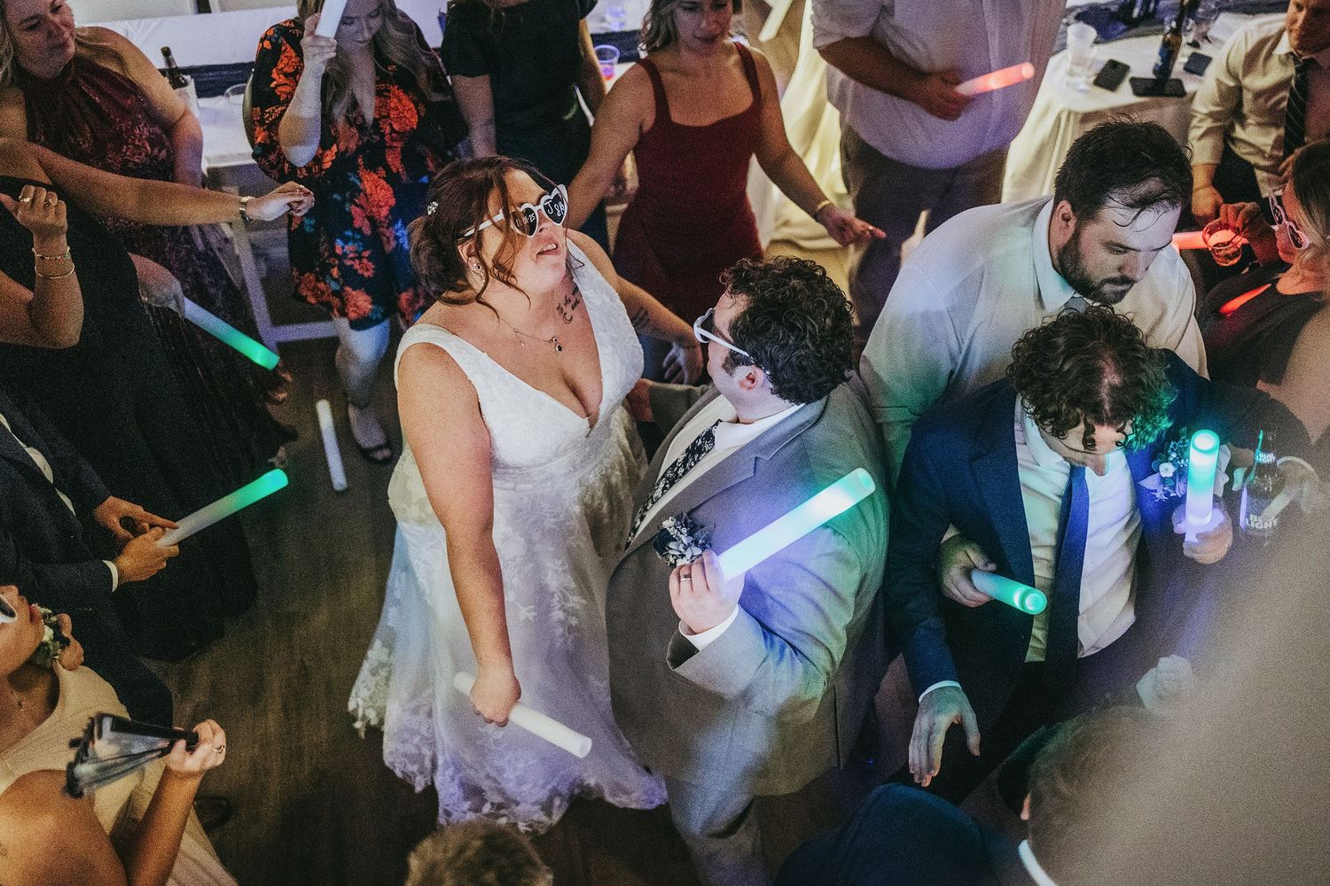 Wedding guests dancing with glow sticks on a dimly lit dance floor.