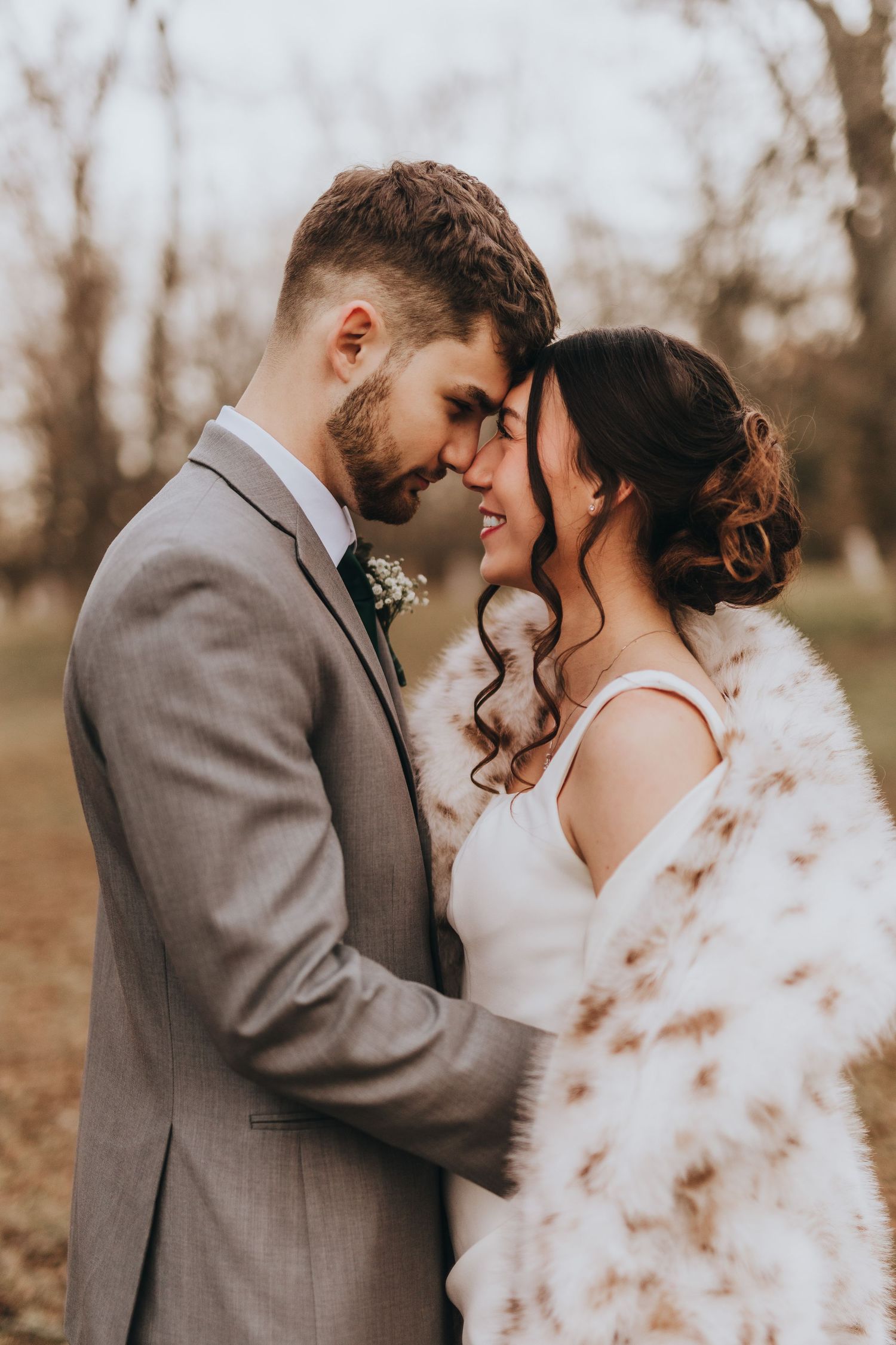 A romantic wedding couple in autumn colors share intimate moments in a series of tender poses wearing grey suit and white dress.