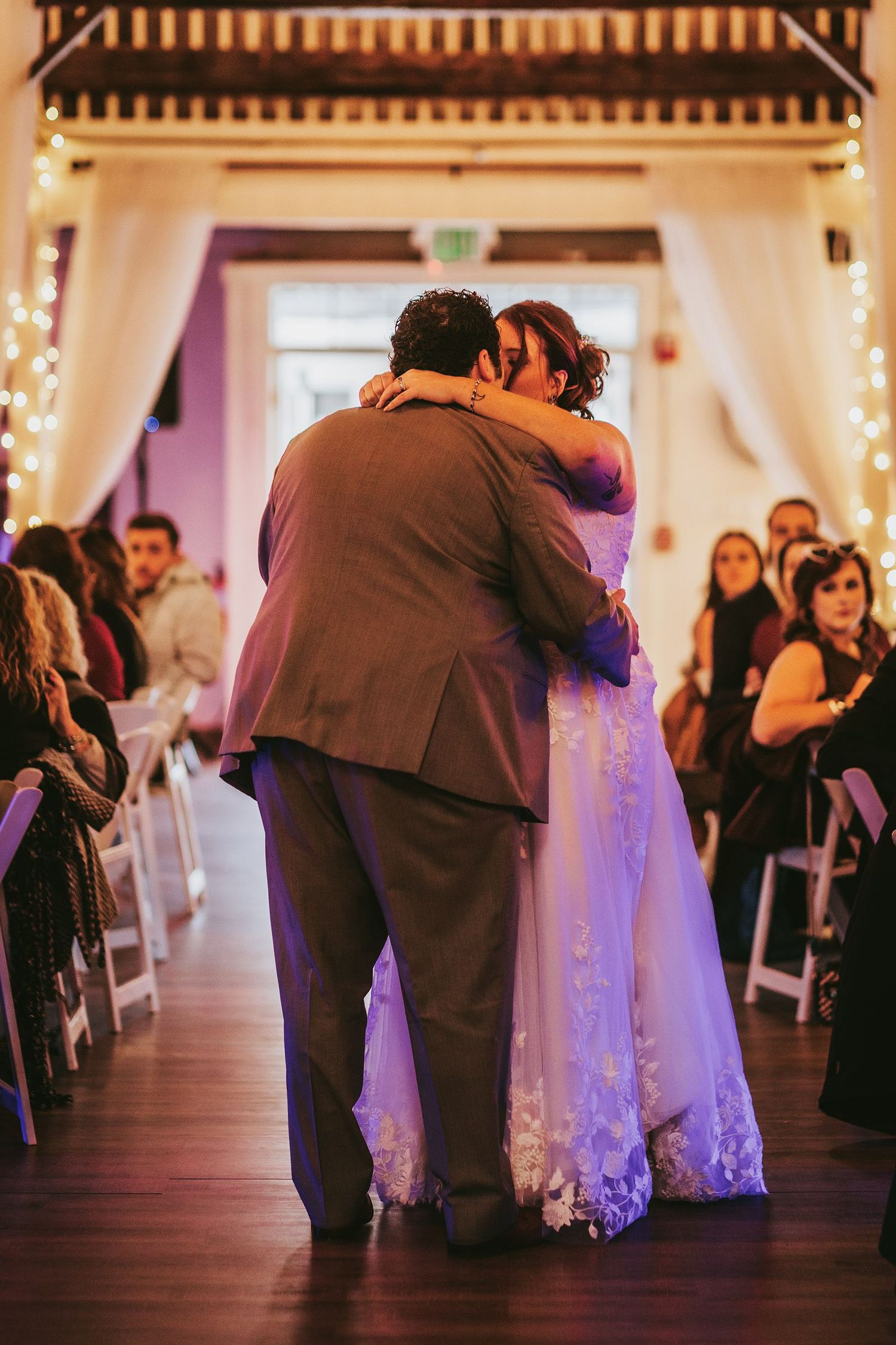 Wedding guests dancing in pairs across a wooden dance floor with string lights overhead.