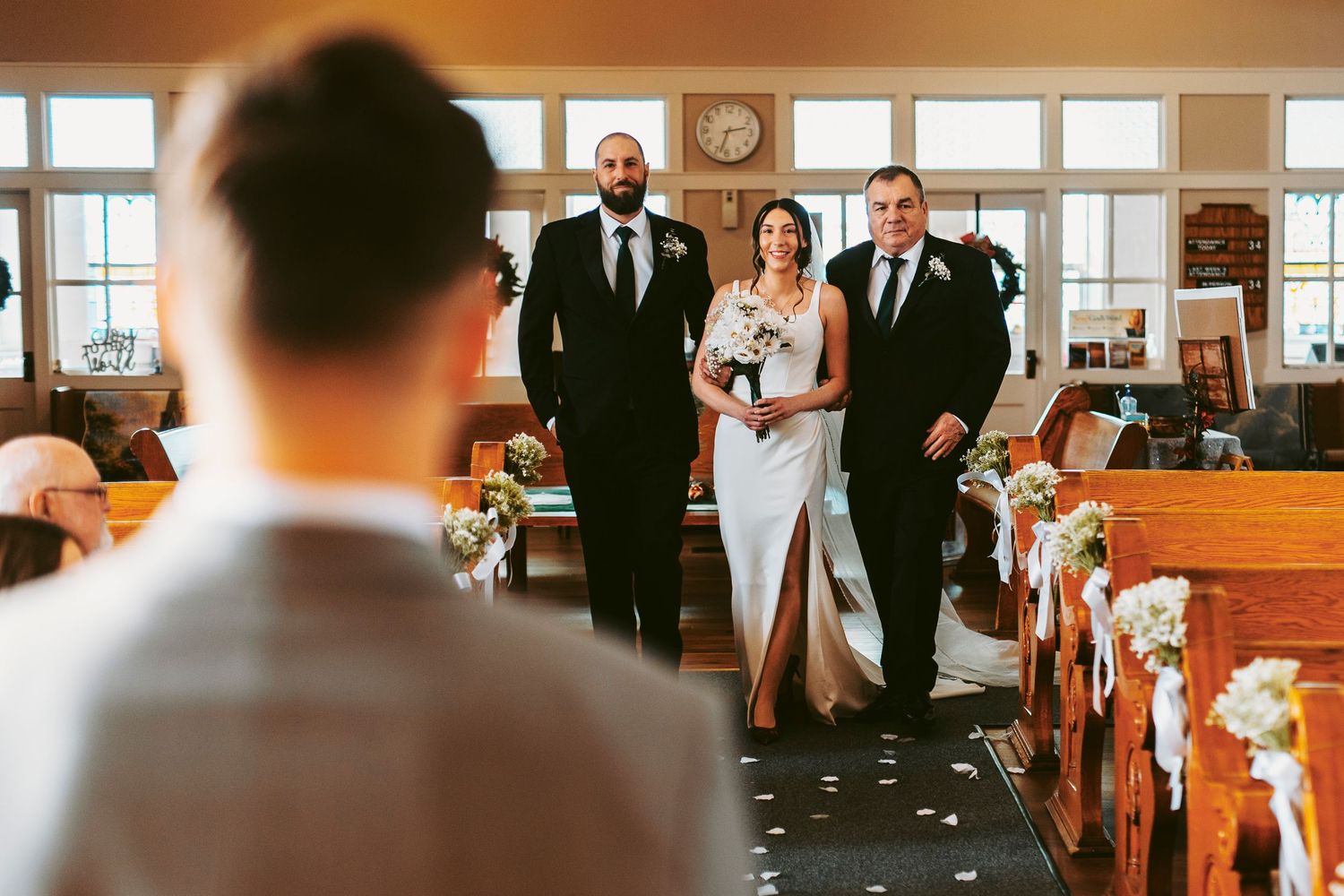 A group of formally dressed guests stand and applaud during an indoor wedding ceremony.