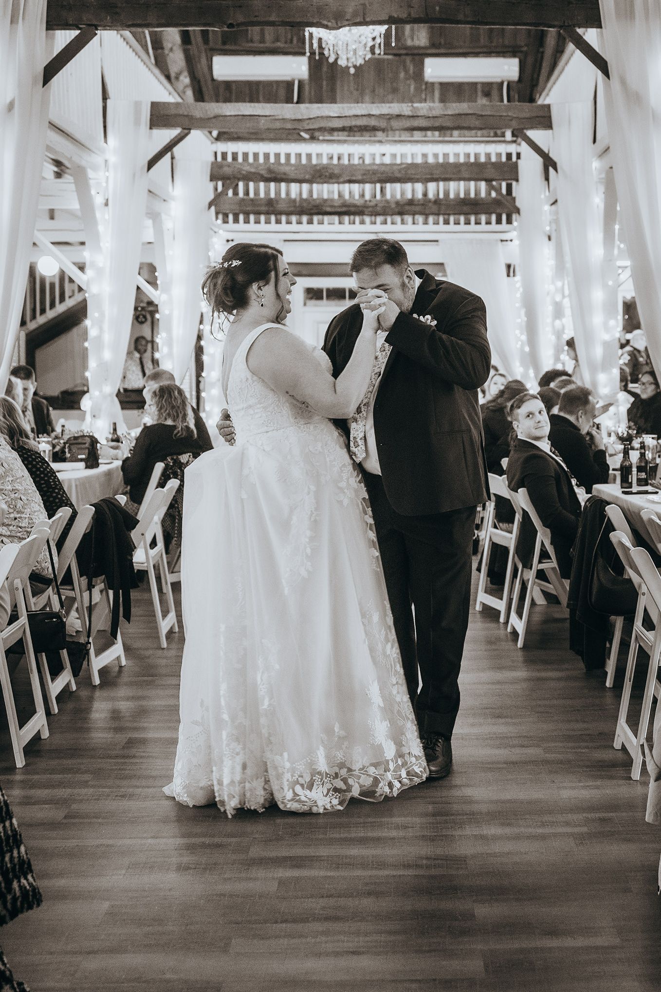 Wedding reception venue with white decor and wooden beams featuring elegant table settings.