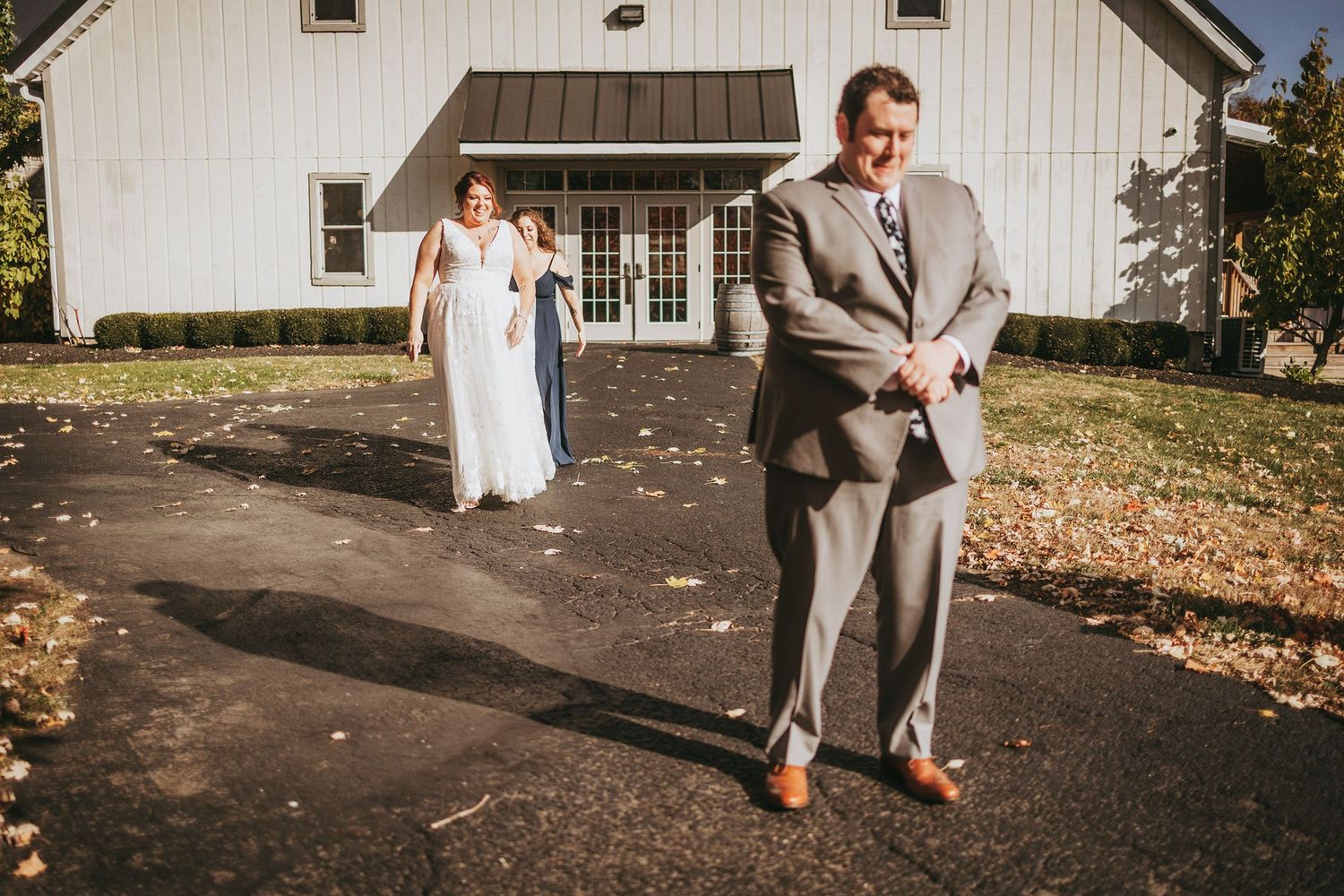 Wedding couple walking together outside white barn building in autumn.