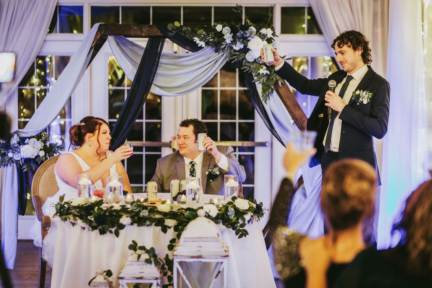 Wedding reception hall adorned with white drapery and twinkling lights.