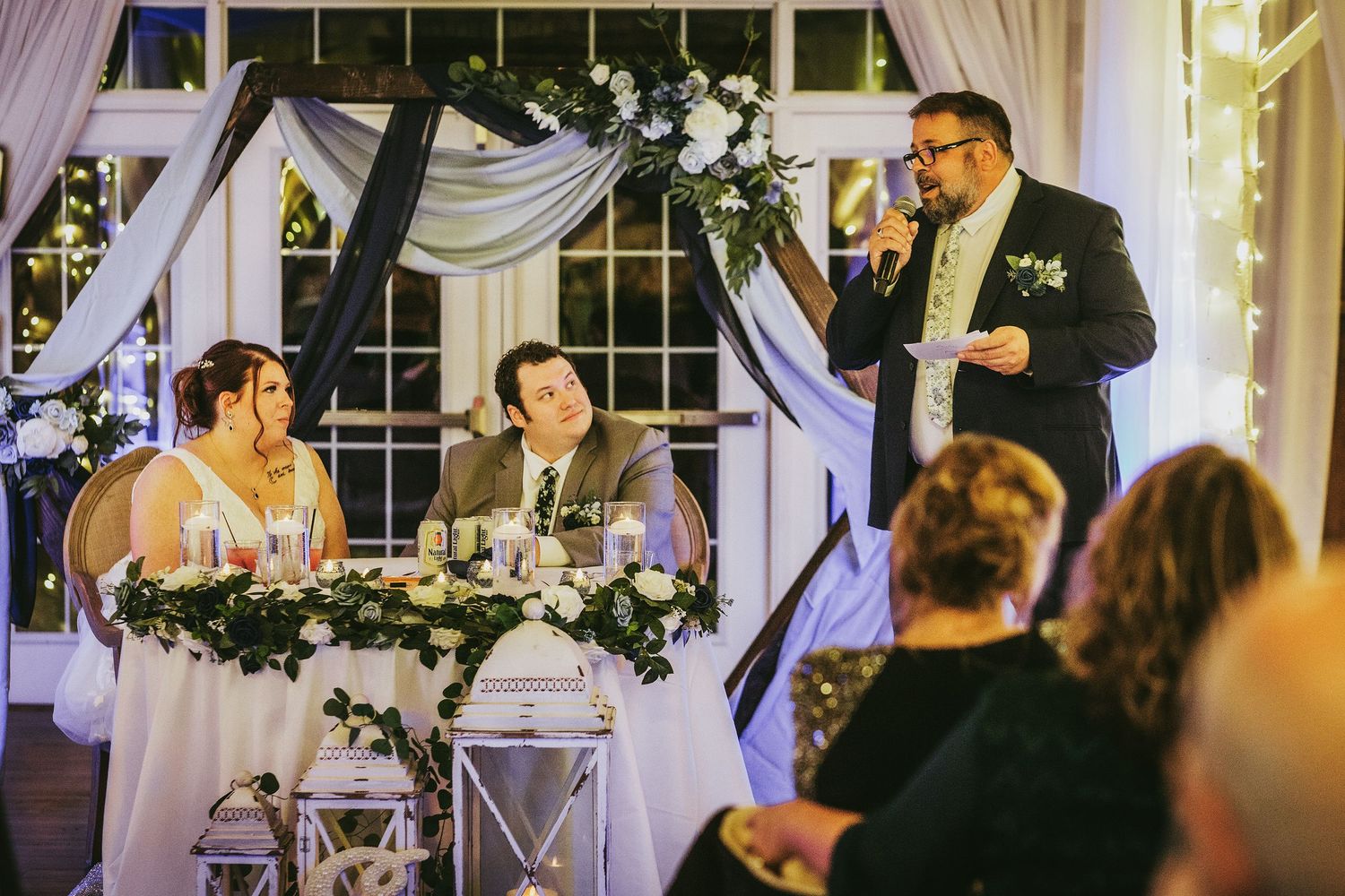 A wedding reception speech being delivered at an elegantly decorated venue with white draping.