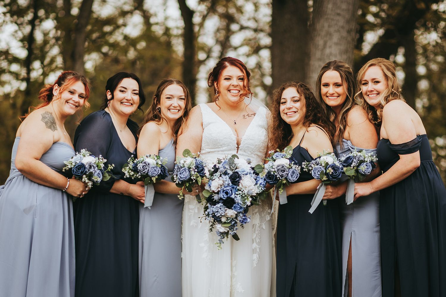 Wedding party wearing navy and grey dresses posing together outdoors.