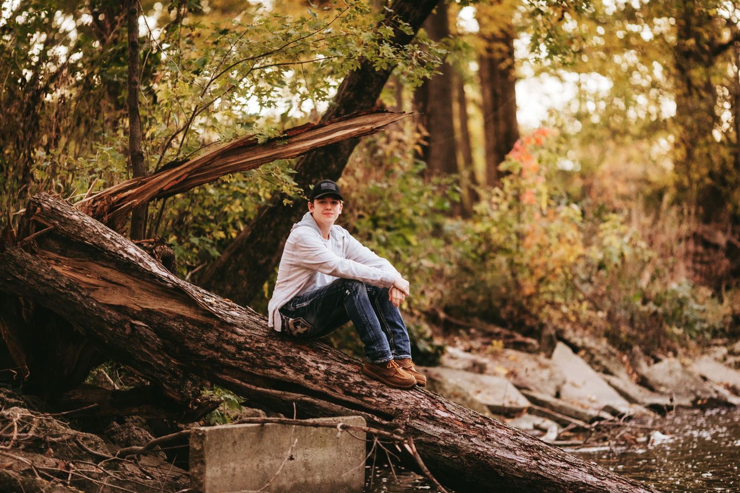 A person sits peacefully on a fallen tree trunk in a sunlit autumn forest.